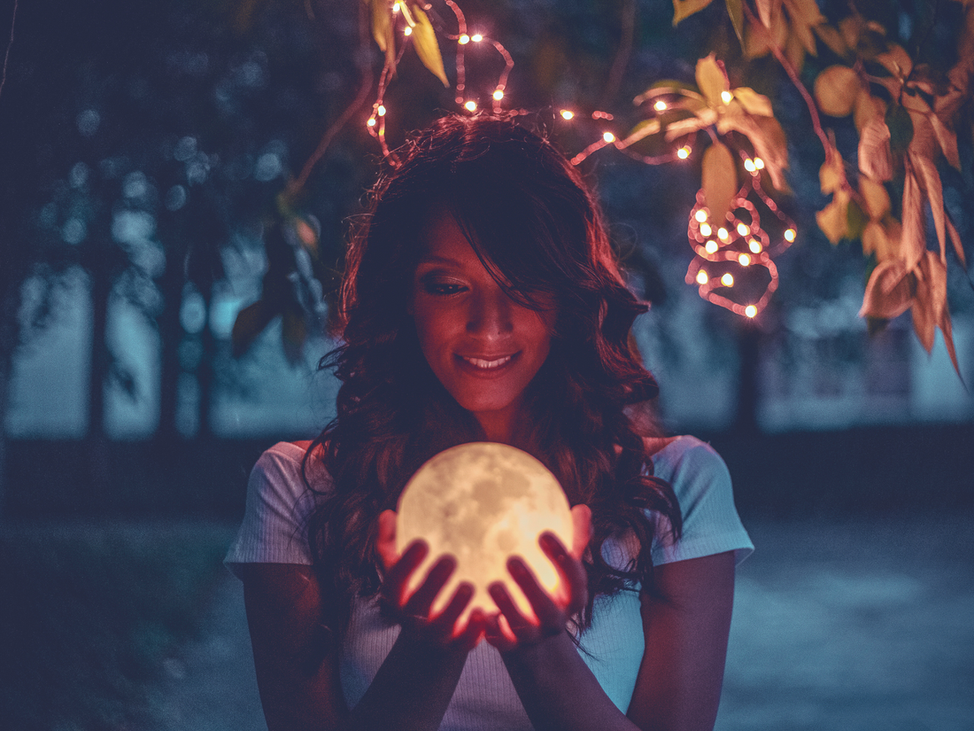 Happy woman holding a glowing full moon in her hands, symbolizing connection to lunar energy.